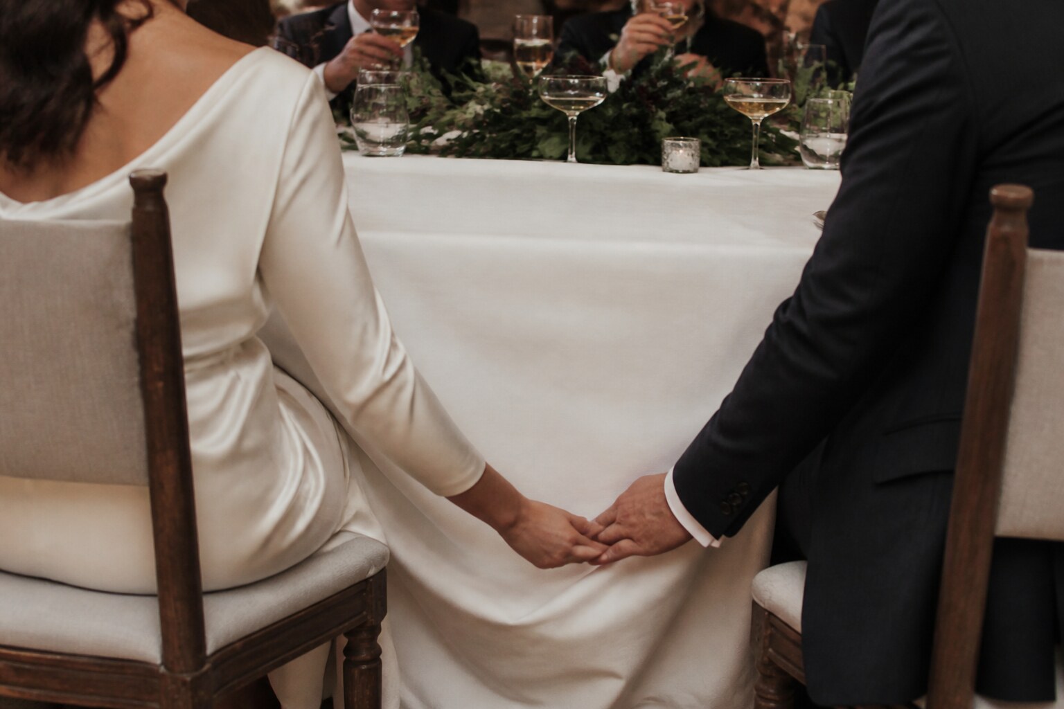 A couple holds hands quietly beneath the wedding table